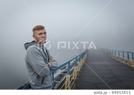 Man in gray hoodie stay on bridge in foggy morning Man in gray hoodie stay on bridge in foggy morning 69952653