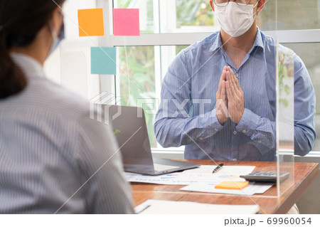Asian business team colleagues wearing mask greeting by looking through the plastic protective wall, concept of social distancing to prevent the spread of coronaviru COVID-19. 69960054