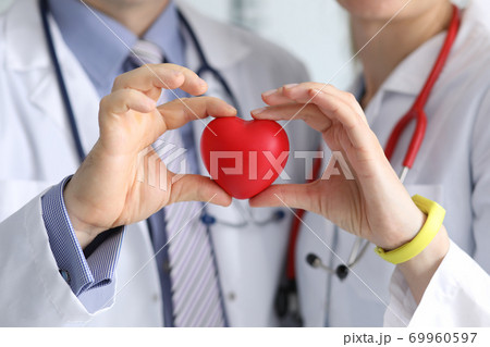 Doctors man and woman with phonendoscope hold red heart in their hand Doctors man and woman with phonendoscope hold red heart in their hand 69960597