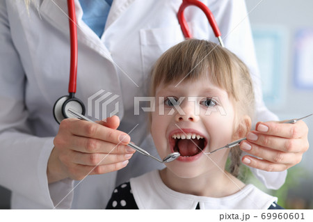 Dentist doctor with stethoscope examines teeth of little girl in clinic Dentist doctor with stethoscope examines teeth of little girl in clinic 69960601