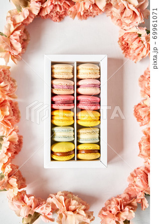 round beautiful sweets macaroni in a festive box with flowers on a flowers background. Still life with macaroni cakes and different flower. 69961071