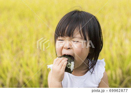 稲穂の実った秋の田んぼで美味しい新米おにぎりを食べる子供 69962877