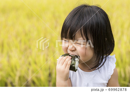 稲穂の実った秋の田んぼで美味しい新米おにぎりを食べる子供 69962878