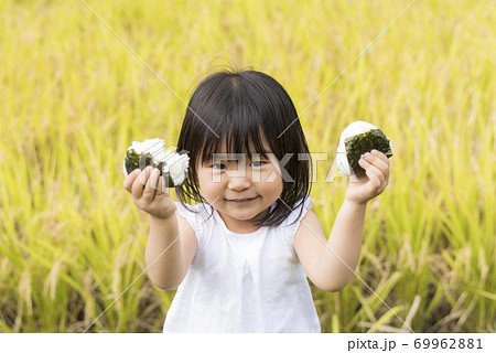 稲穂の実った秋の田んぼで美味しい新米おにぎりを食べる子供 69962881