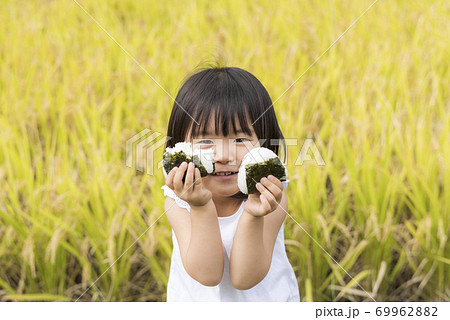 稲穂の実った秋の田んぼで美味しい新米おにぎりを食べる子供 69962882