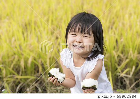 稲穂の実った秋の田んぼで美味しい新米おにぎりを食べる子供 69962884