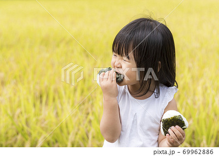 稲穂の実った秋の田んぼで美味しい新米おにぎりを食べる子供 69962886