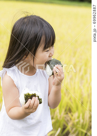稲穂の実った秋の田んぼで美味しい新米おにぎりを食べる子供 69962887