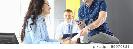 Businesswoman and businessmen in office are sitting at table, smiling and discussing work processes Businesswoman and businessmen in office are sitting at table, smiling and discussing work processes 69970381