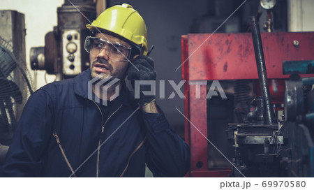 Factory worker talking on portable radio while inspecting machinery parts 69970580