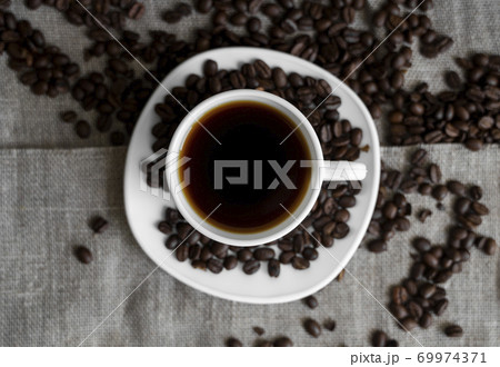 Coffee cup with roasted coffee beans on linen background. Mug of black coffe with scattered coffee beans. Fresh coffee beans. 69974371