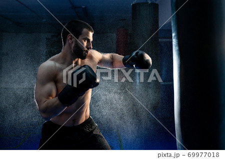 Powerful male boxer with punching bag for uppercut training Powerful male boxer with punching bag for uppercut training 69977018
