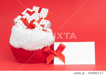 Heaps of christmas gifts in Santa Claus sack wrapped in gift paper polka with festive ribbon on red background with note mock up. Heaps of christmas gifts in Santa Claus sack wrapped in gift paper polka with festive ribbon on red background with note mock up. 69980315
