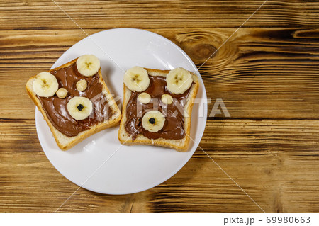 Two sweet sandwiches with delicious chocolate hazelnut spread and banana in shape of bear on wooden table. Top view 69980663