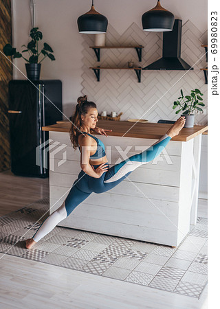 Fit woman doing front split standing with one foot on the floor and the other placed on the table. 69980823