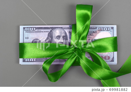 Hundred dollar bill tied with green bow on grey background. Money, gift wrapped in green bow and ribbon, US currency, cash, business success, bonus, monetary prize, luck in the game concept Hundred dollar bill tied with green bow on grey background. Money, gift wrapped in green bow and ribbon, US currency, cash, business success, bonus, monetary prize, luck in the game concept 69981882