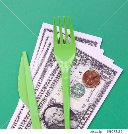 Disposable plastic cutlery green. Plastic fork and knife lie on a small amount of US dollars 69983894