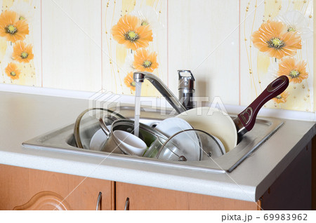 Dirty dishes and unwashed kitchen appliances lie in foam water under a tap from a kitchen faucet Dirty dishes and unwashed kitchen appliances lie in foam water under a tap from a kitchen faucet 69983962
