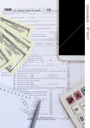 Composition of items lying on the 1040 tax form. Dollar bills, pen, calculator, smartphone, paper clip and notepad. The time to pay taxes 69984465