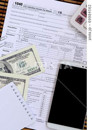 Composition of items lying on the 1040 tax form. Dollar bills, calculator, smartphone, paper clip and notepad. The time to pay taxes Composition of items lying on the 1040 tax form. Dollar bills, calculator, smartphone, paper clip and notepad. The time to pay taxes 69984562