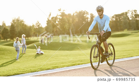 Active lifestyle. Young athletic man in sportswear and protective helmet riding mountain bike in park during sunset Active lifestyle. Young athletic man in sportswear and protective helmet riding mountain bike in park during sunset 69985735