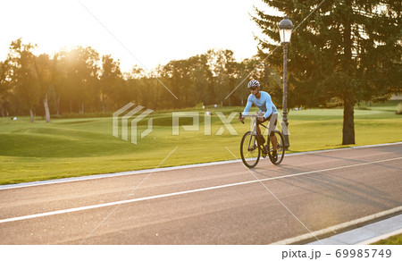 Athletic man in sportswear cycling in city park at sunset, riding bicycle along a road 69985749