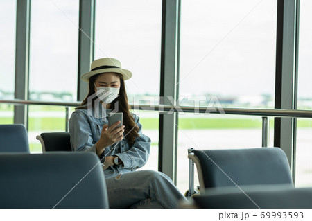 Asian young woman traveller wearing face maks using mobile phone at airport Due Covid-19 flu virus pandemic and protection 69993593
