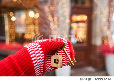 Christmas mood in blurred background. Hand in red mitten holding key with house shaped keychain. Mortgage or rent concept. 69994248