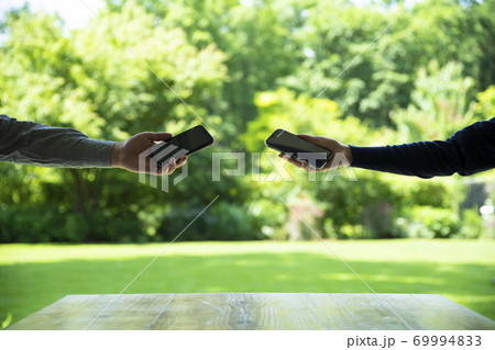スマホをかざし合う男女の手 69994833