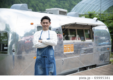 キッチンカーの前に立つ若い男性スタッフ キッチンカーの前に立つ若い男性スタッフ 69995381