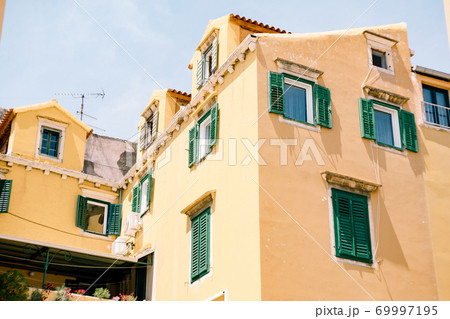 Large beige residential building with windows and green shutters on a sunny day. Large beige residential building with windows and green shutters on a sunny day. 69997195