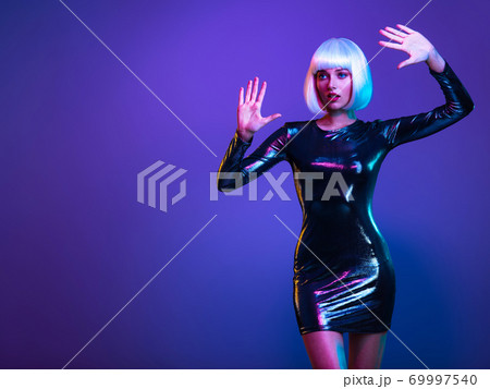 Full-length portrait of the beautiful woman with lifted hands up near face. Art portrait of an young attractive model. Fantasy style. Glamour fashion girl. Stylish blonde in shiny dress. Full-length portrait of the beautiful woman with lifted hands up near face. Art portrait of an young attractive model. Fantasy style. Glamour fashion girl. Stylish blonde in shiny dress. 69997540