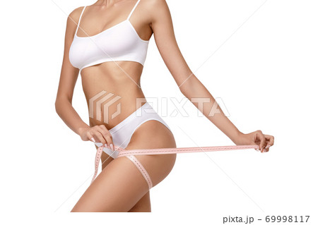 Slim tanned woman's body over gray background - waist measurement 69998117