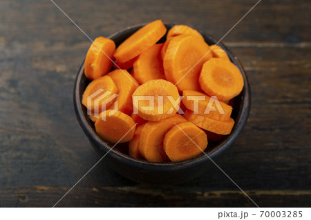 Sliced carrots in a bowl on a wooden background. Vegetable, ingredient and staple food. 70003285