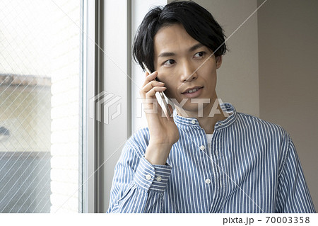 窓際で電話をする若い男性 窓際で電話をする若い男性 70003358