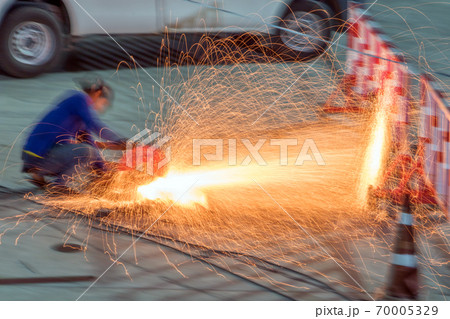A man cuts steel with a red sparkle flying from cut metal material.  70005329