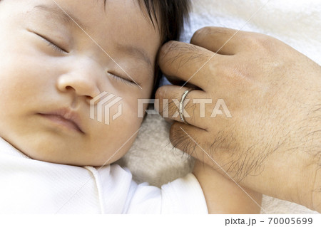 寝ている赤ちゃんと 赤ちゃんの手を握る男性の手の写真素材