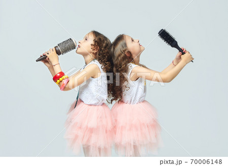 two little girls comb each other's hair. twin sisters singing into hair brushes. white background 70006148