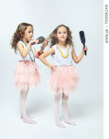 two little girls comb each other's hair. twin sisters singing into hair brushes. white background 70006149