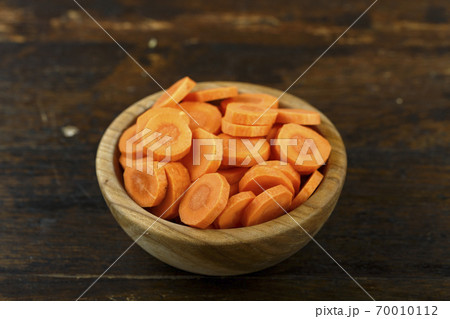 Sliced carrots in a bowl on a wooden background. Vegetable, ingredient and staple food. 70010112
