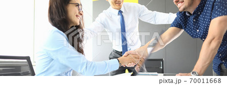 Businessmen and businesswoman in their office smiling and shaking hands 70011668