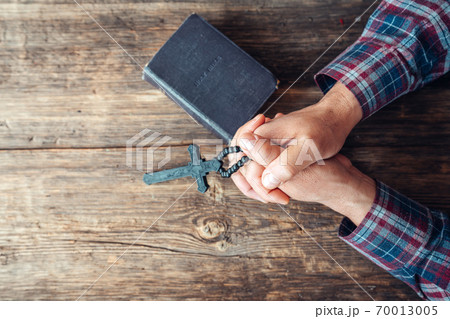 Hands are holding a crucifix and an old hard covered holly Bible and praying on a rustic wooden background. 70013005