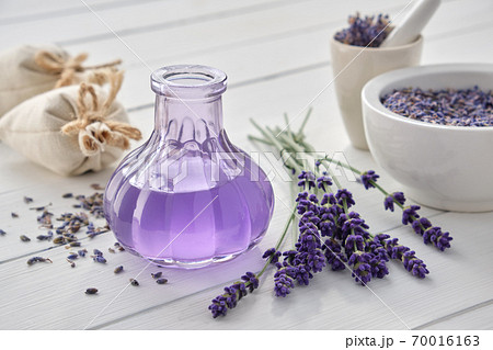 Dry lavender flowers, bottle of essential oil or flavored water, sachet and mortar on white wooden table. 70016163