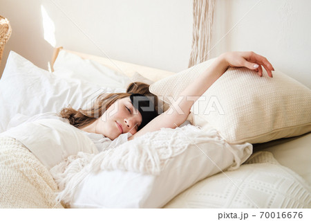 Young beautiful girl lying in comfortable bed wearing sleep mask in the morning at cozy room. Concept of rest at home, sleep, insomnia, self-isolation, stay home during quarantine, pandemic. 70016676