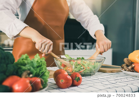 Asian woman is mixing the ingredients in a salad bowl at the kitchen cooking table. Asian woman is mixing the ingredients in a salad bowl at the kitchen cooking table. 70024833