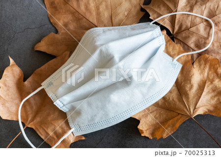 Covid-19 protective mask on dry autumn leaves background 70025313