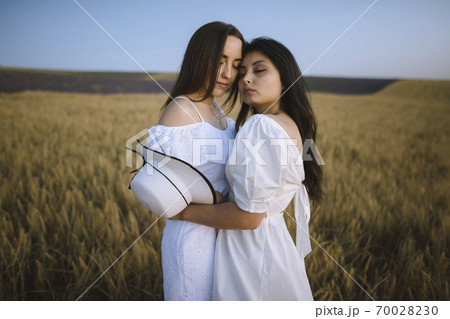 France, Women in white dresses embracing in field 70028230