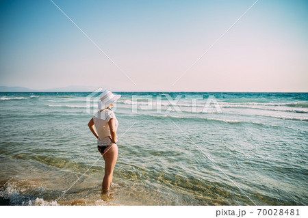Young Caucasian Lady Woman In Swimsuit And Summer Hat Standing In Sea. Vacation On Sea Ocean Beach Young Caucasian Lady Woman In Swimsuit And Summer Hat Standing In Sea. Vacation On Sea Ocean Beach 70028481
