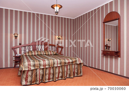 A hotel with old fashioned retro styled rooms, a bedroom with checked bedding, striped wallpaper and mirror. A hotel with old fashioned retro styled rooms, a bedroom with checked bedding, striped wallpaper and mirror. 70030060