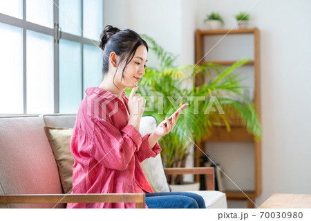 ソファでくつろぎながらスマホを操作する女性。 70030980